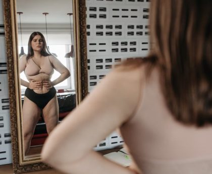 Woman in underwear looking at her reflection in a mirror, contemplating body image.