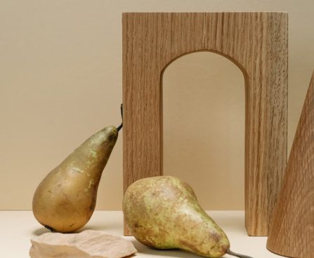 A minimalist still life composition featuring pears with geometric wooden shapes on a beige background.